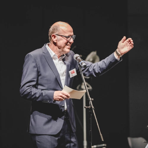 Mensch spricht mit einem Mikrofon zu einem Publikum